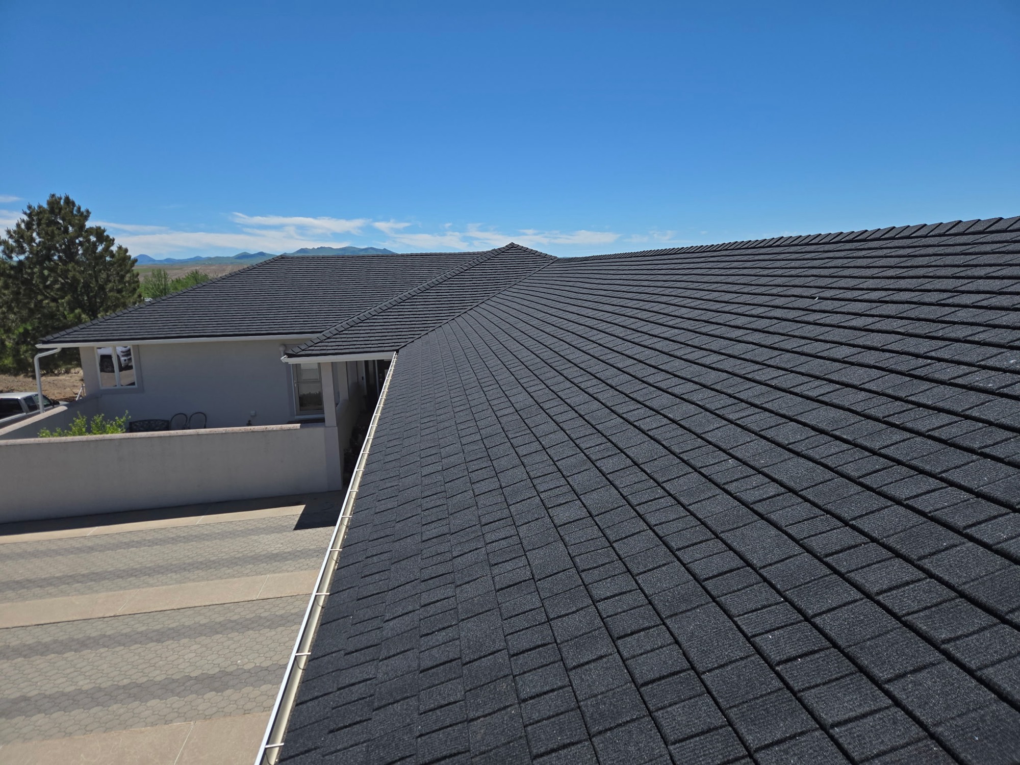 Finished WeatherLok stone-coated steel roof on a single story home, seen along the roof plane with the interlocking courses running up to the ridge and mountains in the distance.