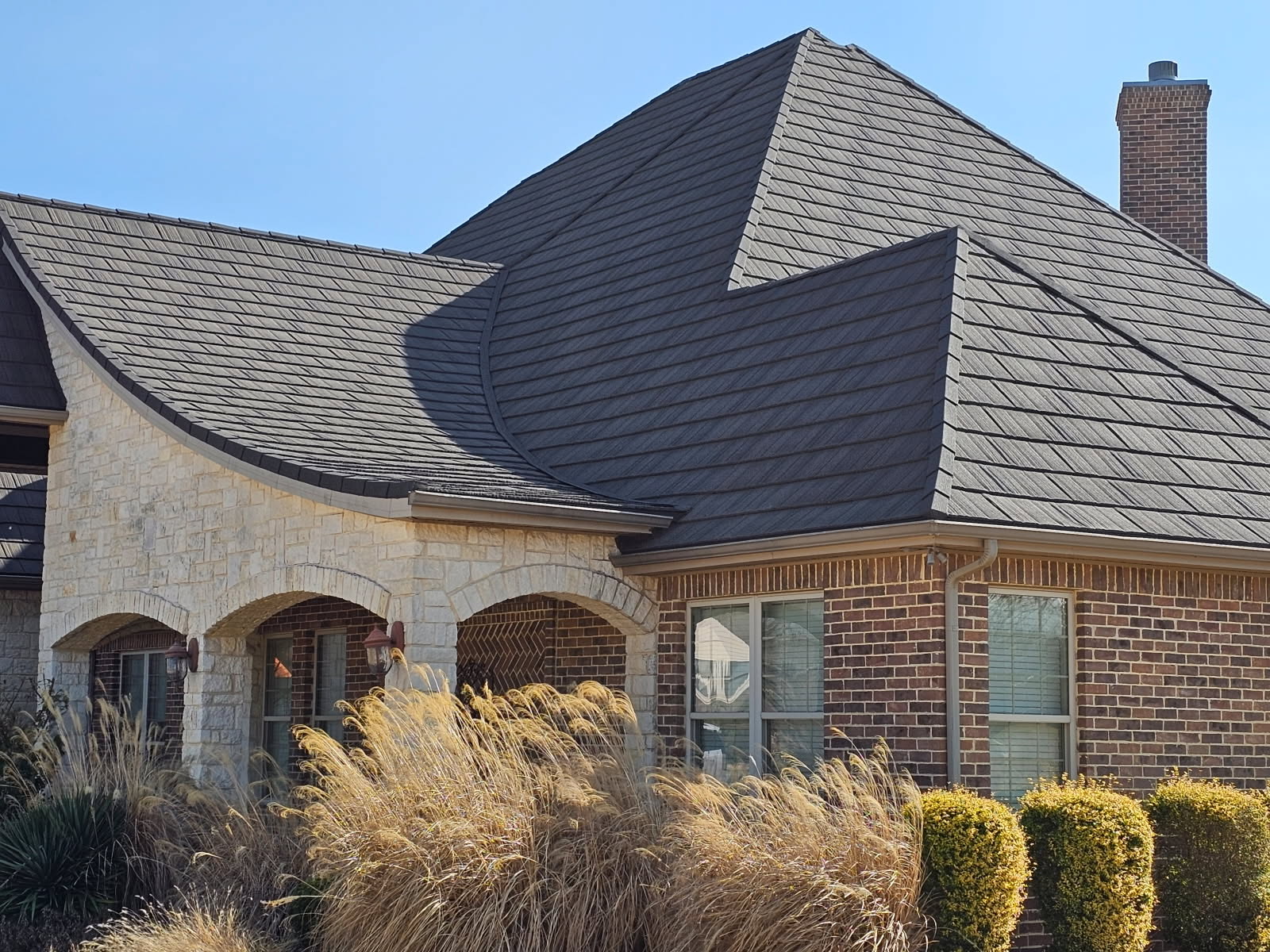 A charcoal WeatherLok stone-coated steel shake roof on a stone and brick home under a clear sky